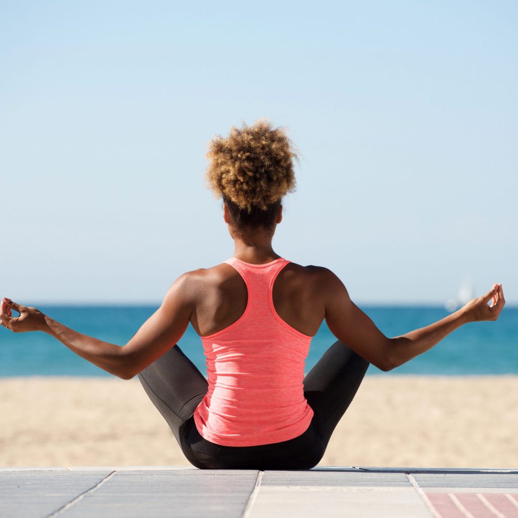 a young woman doing yoga on a beach and facing the ocean