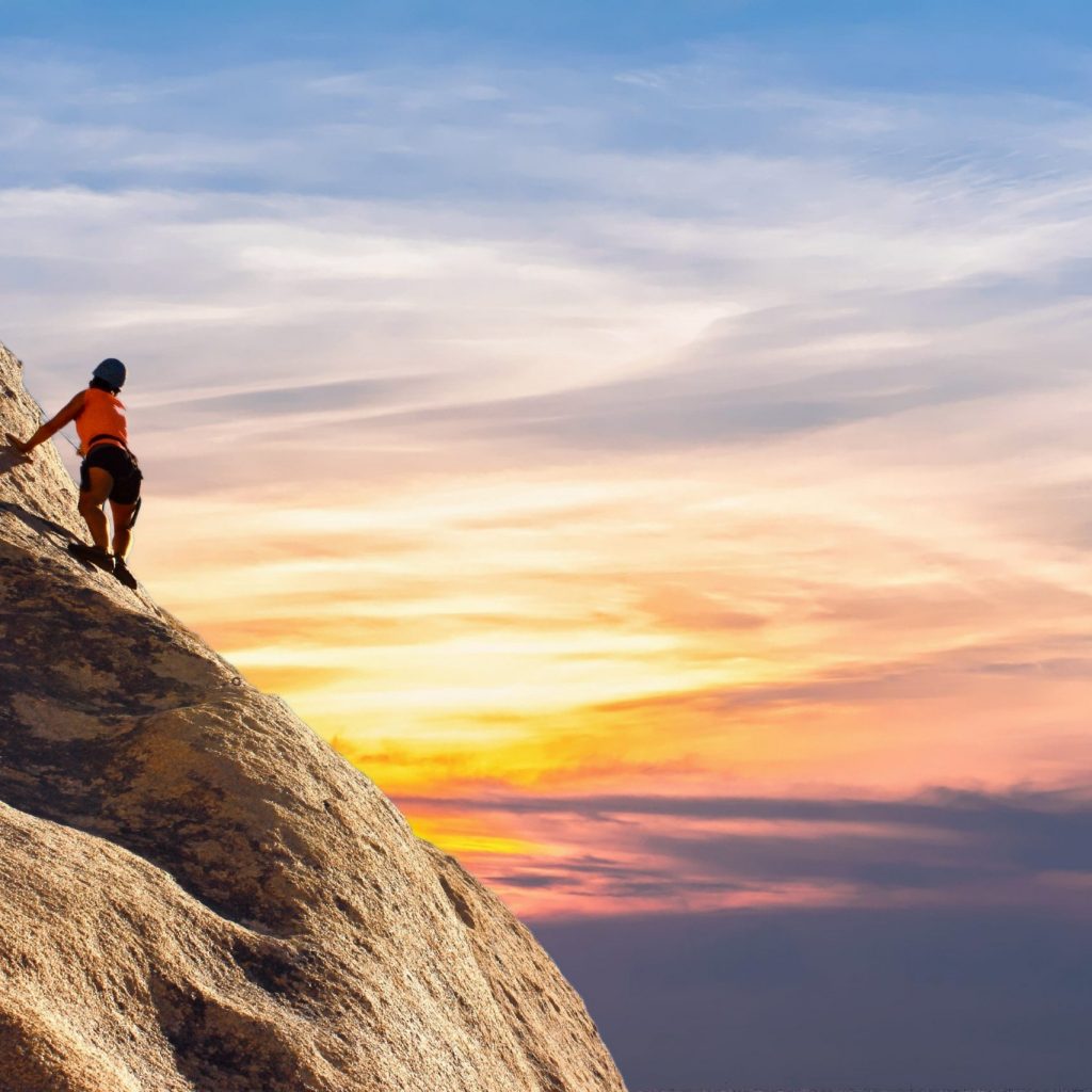 a man rock climbing is going up the rock as the sun sets